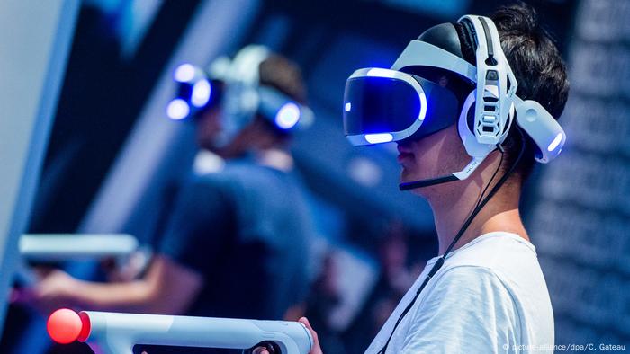 A young man wearing a virtual reality headset points a gun like device at a screen A young man wearing a virtual reality headset points a gun like device at a screen