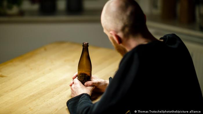 Muškarac sjedi za stolom s bocom piva u rukama