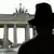 A man in a flop hat faces away from the camera at the Brandenburg Gate