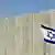 An Israeli flag waves in front of the wall between Israel and the Palestinian territory