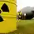 A canister bearing the radioactive symbol is seen with a bomb in the background