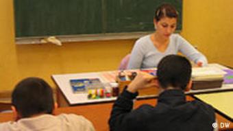 A teacher sitting in a classroom in front of two students