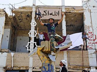 A rebel fighter on top a statue gestures as fighters celebrate overrunning Moammar Gadhafi's compound
