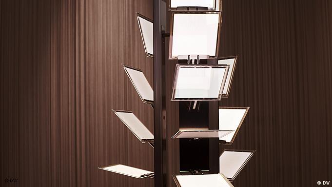 Bu fotoğrafta Kahverengi bir perdenin önünde, üzerine esnek bir şekilde birkaç parlak ışıklı ve yarı saydam beyaz diskin tutturulduğu metal çerçeve gösteriliyor