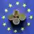 Razne kovanice eura usred simbola EU-a, leže na zastavi EU-a