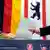 Ein Wähler steckt in Berlin seine Stimmen zur Wahl des Abgeordnetenhauses in eine Wahlurne; im Hintergrund sind die schwarz-rot-goldene Deutschland-Fahne und die rot-weiße Berliner Fahne mit dem schwarzen Wappentier, einem Bär, zu sehen (Foto: dpa)