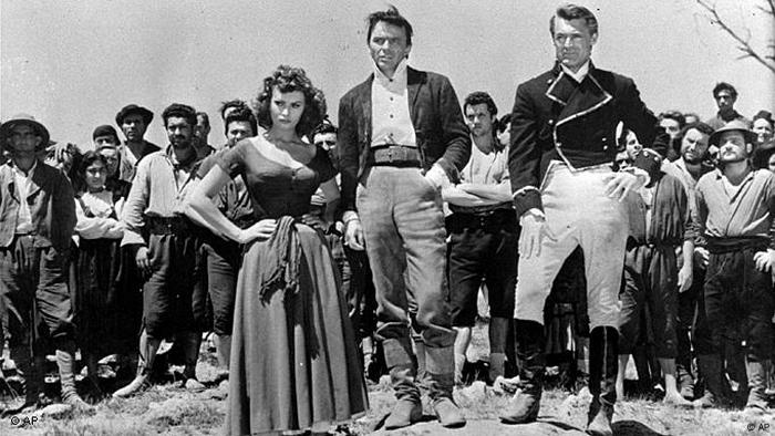 Sophia Loren steht mit zwei uniformierten Männern vor eine Gruppe von Männern.