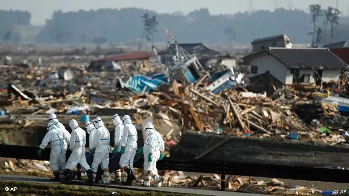 Japanese police officers carry a body during search and recovery operation for missing victims in the area devastated by the March 11 earthquake and tsunami in Namie, Fukushima Prefecture, northeastern Japan, Friday, April 15, 2011. In the background is part of the Fukushima Dai-ichi nuclear complex.(AP Photo/Hiro Komae)