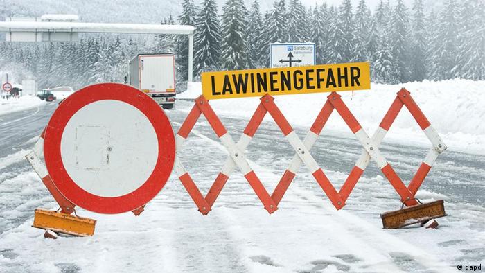 Auf einer zugeschneiten Straße warnt ein Schild vor Lawinengefahr