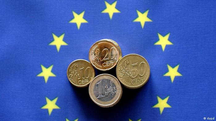 Монеты в 10, 20, 50 евроцентов и 1 евро на фоне флага Евросоюза