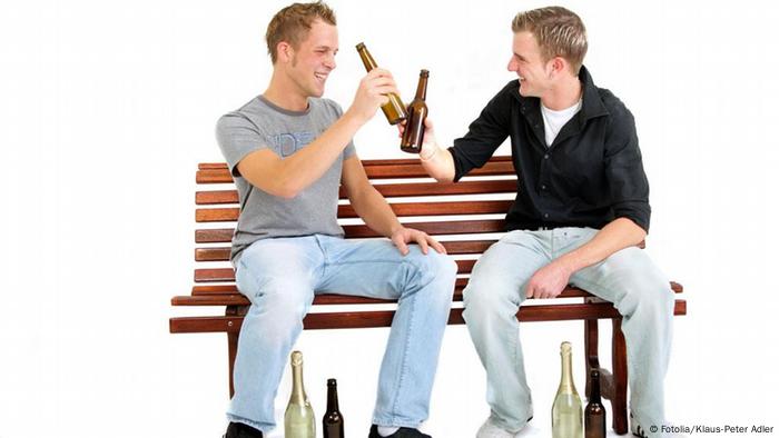 Zwei junge Männer sitzen auf einer Bank und stoßen mit Bierflaschen an