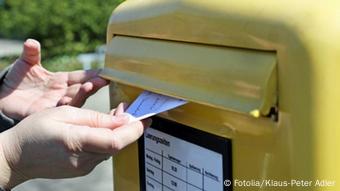 Ein Brief wird in einen gelben Briefkasten gesteckt