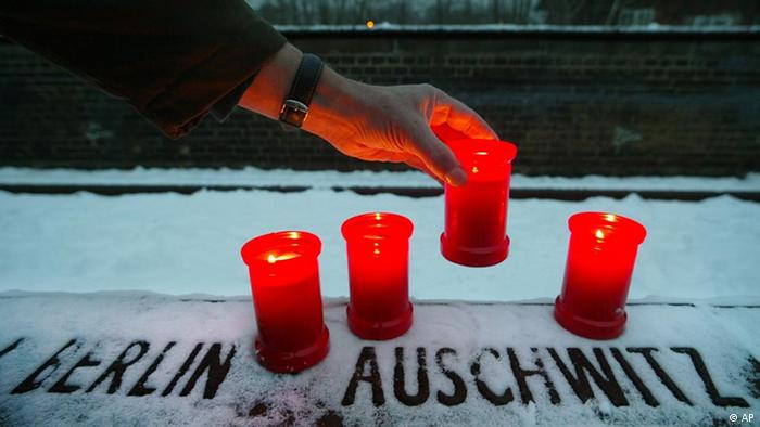 Candles being set on a stone plaque commorating Auschwitz