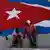 People sit under a mural of a Cuban flag in Havana, Cuba.