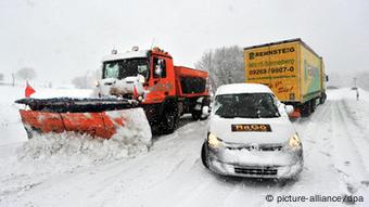 Laster und PKW sowie ein Räumfahrzeug auf einer verschneiten Straße