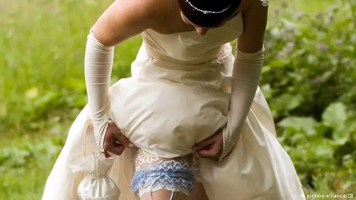 Eine Braut in einem weißen Hochzeitskleid zupft an ihrem blauen Strumpfband