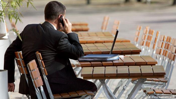Ein Geschäftsmann im Anzug sitzt auf Gartenstühlen in einem Berliner Biergarten mit Akten und Laptop auf dem Tisch und telefoniert mit einem Mobiltelefon , aufgenommen am 23.04.2007. Foto: Arno Burgi +++(c) dpa - Report+++
