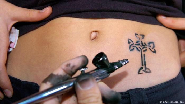 Kobieta robi sobie tatuaż z krucyfiksem w pobliżu pępka