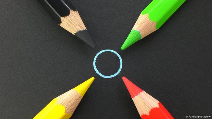 Un crayon noir, un jaune, un vert et un rouge sur un tapis noir, ciblant un cercle bleu
