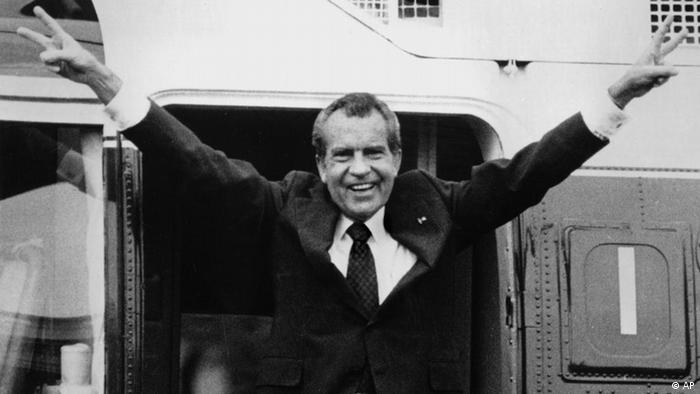 Schwarz-weiß Foto von Richard Nixon: Er streckt die Arme von sich und zeigt mit beiden Händen das Siegeszeichen. 