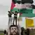 Palestinian protesters hold flags as they stand on a vehicle partly covered by a banner depicting jailed Islamic Jihad leader Khader Adnan, during a weekly demonstration against the controversial Israeli barrier, in the West Bank village of Bilin near Ramallah February 17, 2012. Several thousand Palestinians rallied in Gaza and the West Bank on Friday in support of Adnan, who is on the 62nd day of a hunger strike to protest his detention by Israel. REUTERS/Ammar Awad (WEST BANK - Tags: POLITICS CIVIL UNREST)