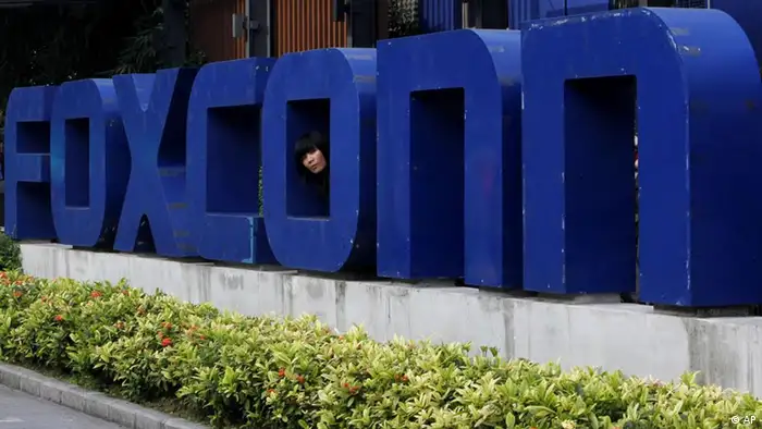 A worker looks out through the logo at the entrance of the Foxconn complex in the southern Chinese city of Shenzhen Thursday, May 27, 2010. A young man became the 10th worker to jump to his death at a Foxconn Technology Group factory in the city, just hours after the company's chairman toured the plant that makes iPods and other top-selling gadgets, state-run media said. (AP Photo/Kin Cheung)