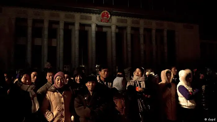 People stand in front of the Great Hall of the People, where the opening session of the annual National People's Congress will be held, as they wait for the Chinese flag to be raised on Tiananmen Square, in Beijing, China, early Monday morning, March 5, 2012. (Foto:Andy Wong/AP/dapd)