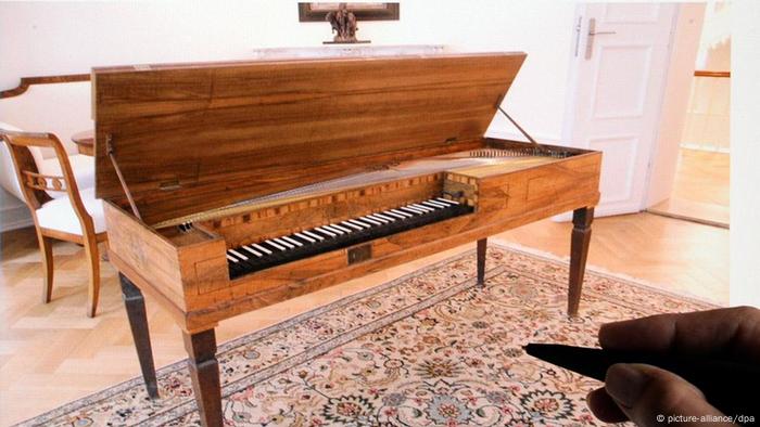 A hand with a pen points on a screen showing a piano standing on an ornamental carpet