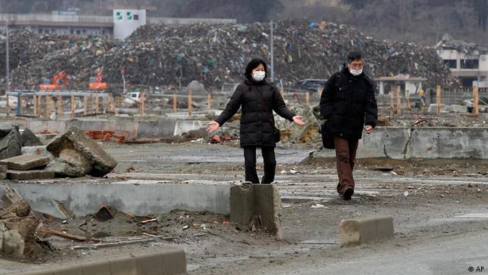 Mann und Frau laufen mit Mundschutz durch zerstörtzes Gebiet in Japan (Foto: AP Photo/Shizuo Kambayashi)