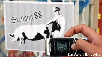 Eine Hand fotografiert mit einer Handy-Kamera einen Aufkleber mit Aufschrift 'Stellung 88' (Foto: dpa)