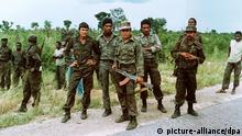 Eine Gruppe kubanischer Soldaten kontrolliert eine Straße nahe Cuito Cuanavale. (Februar 1988). Insgesamt halten sich 40000 Kubaner zur Unterstützung der Regierungsarmee im Land auf. Nach dem Aufstand gegen die portugiesische Kolonialherrschaft erhielt Angola im Januar 1975 seine erste eigene Regierung, an der alle drei Befreiungsbewegungen (MPLA, UNITA, FNLA) beteiligt waren. Noch vor der formellen Unabhängigkeit am 11.11.1975 kam es zu militärischen Auseinandersetzungen zwischen den Gruppen. Die marxistisch orientierte MPLA konnte sich mit sowjetischer und kubanischer Unterstützung gegen die prowestliche Unita und die FNLA durchsetzen und stellte den Staatspräsidenten. Die Kämpfe gingen unvermindert weiter. Ab 1980 erhielt die Unita Unterstützung durch südafrikanische Truppen. Verhandlungen Ende der 80er Jahren führten 1991 zum Friedensvertrag von Estoril. Nach den ersten Mehrparteien-Wahlen 1992 entbrannte der Bürgerkrieg erneut. Schlagworte Politik, Militär, Krisen, Bürgerkrieg, Kuba, Waffen, farbig, Uniform