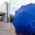 ILLUSTRATION - Ein Frau steht am Dienstag (11.05.2010) im Regen mit einem blauen EU-Schirm vor dem Gebäudekomplex des EU-Parlaments in Brüssel. Das 750-Milliarden-Paket zur Rettung des Euro, dass die EU-Finanzminister am vergangenen Wochenende beschlossen haben, soll als Rettungsschirm für die Stabilität der Gemeinschaftwährung fungieren. Foto: Thierry Monasse