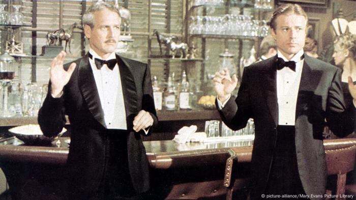 Robert Redford und Paul Newman tragen in einer Szene des Films Der Clou Smokings und halten ihre Hände in die Höhe.