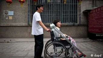 In this photo taken on June 30, 2010, Ni Yulan on a wheelchair is helped by her husband Dong Jiqin outside a temporary lodging in a hotel in Beijing. Ni, a former lawyer and veteran activist left disabled by past police mistreatment, went on trial Thursday, Dec. 29, 2011, the third dissident in a week to be prosecuted as China presses a sweeping crackdown to deter popular uprisings like the ones that shook the Arab world. (AP Photo/Andy Wong)