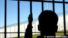 Ein Journalist steht mit einer Hand am Gitter einer Zelle der neuen Justizvollzugsanstalt im bayerischen Kempten am 4.9.2003. Er blickt auf Überwachungsanlagen mit Kameras und einer meterhohen Mauer mit Zaun. Wenige Wochen vor der Inbetriebnahme der JVA Kempten erhielten Journalisten die Möglichkeit, unter realitätsnahen Bedingungen eine Nacht hinter Gittern zu verbringen. Neben der obligatorischen Gefangenenkleidung mussten sie sich auch dem Tagesablauf in einer JVA unterordnen. Die JVA in Kempten mit 338 Haftplätzen wurde für mehr als 40 Millionen Euro errichtet und nimmt ab Oktober ihren regulären Betrieb auf.