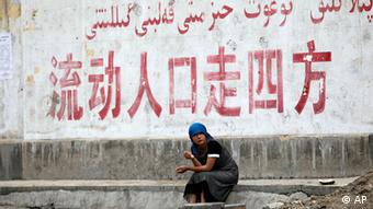 China Frau mit Kopftuch in Xinjiang vor Mauer mit Schriftzeichen