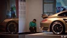 A cleaner takes a nap near a Porsche car at a showroom in Beijing Friday, Dec. 9, 2011. (AP Photo/Andy Wong)