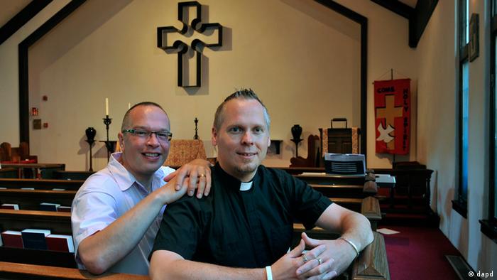 Ein Pfarrer und ein weiterer Mann sitzen in einer Kirche