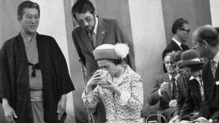 Queen Elizabeth II drinks from a large cup of tea during a ceremony in 1975.