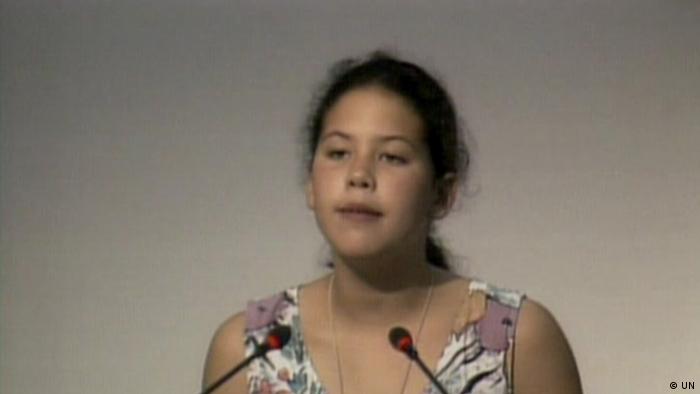 A young girl stands at a lectern with two mikes pointed at her