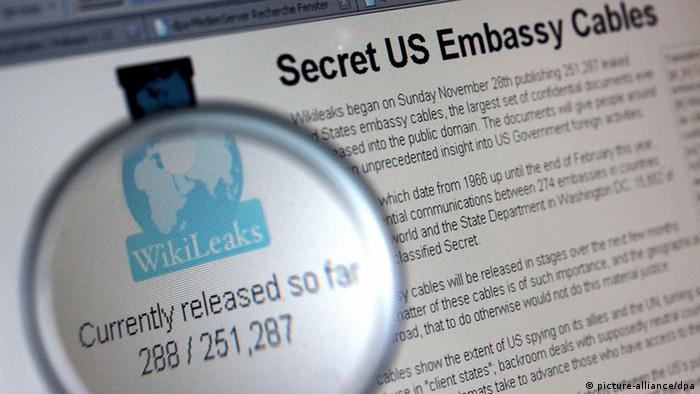 Durch eine Lupe ist am 30.11.2010 das Symbol der Internet-Enthüllungsplatform Wilileaks zu erkennen. Im Hintergrund ist ein Hinweis auf die Wikileaks-Veröffentlichung von US-Botschaftsdepeschen zu sehen.