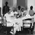 Funcionários coloniais alemães no Togo sentados em mesa e africanos em pé atrás