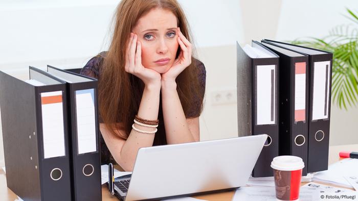 Eine Frau sitzt erschöpft im Büro vor ihrem Computer. Sie hat den Kopf auf die Hände gestützt.