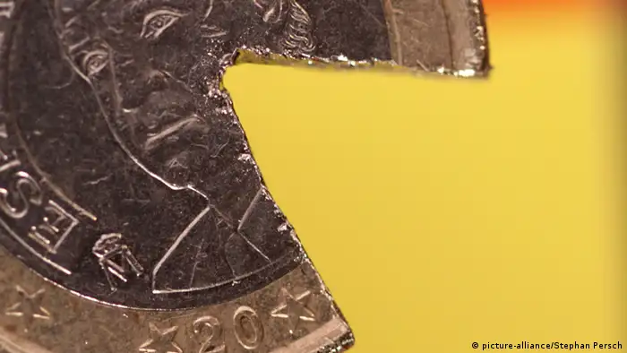 Eine kaputte Ein-Euro-Münze mit dem Bild von Juan Carlos vor der spanischen Flagge