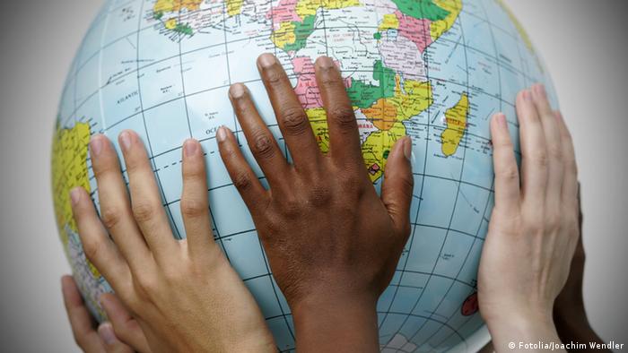 Photo shows several hands holding a large globe