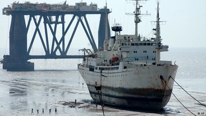 Workers walk past a decommissioned ship, and a oil drilling ship, waiting to be dismantled at a ship breaking yard in Alang, in the western Indian state of Gujarat, Monday, March 13, 2006. After spending 20 to 30 years on the high seas, ships some as tall as 15-story buildings and as long as several football fields, make their way to beaches across South Asia to be dismantled. (AP Photo/Ajit Solanki)