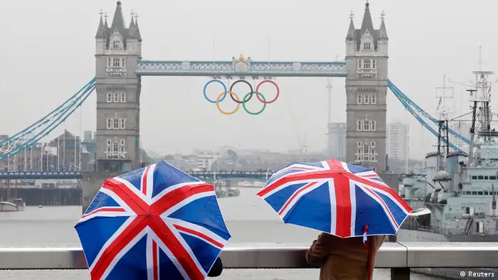Two tourists stand under Union flag umbrellas as they take pictures from London Bridge, of Tower Bridge adorned with the Olympic rings, on a wet summer's morning in central London July 6, 2012. Many parts of Britain are due to receive an average month's rainfall in the next 24 hours, according to local forecasters. REUTERS/Andrew Winning (BRITAIN - Tags: ENVIRONMENT SPORT OLYMPICS)
