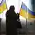 Женщина бросает бюллетень в урну для голосования на фоне украинских флагов.
