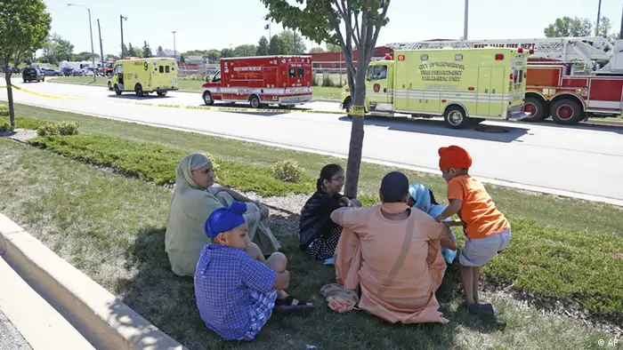 Bystanders sit in the shade at the scene of a shooting inside The Sikh Temple in Oak Creek, Wis, Sunday, Aug 5, 2012. Greenfield Police Chief Bradley Wentlandt says tactical officers have been through the temple where shots were fired about 10:30 a.m. Sunday. He says they found four people inside the building and three people outside. (Foto:Jeffrey Phelps/AP/dapd)