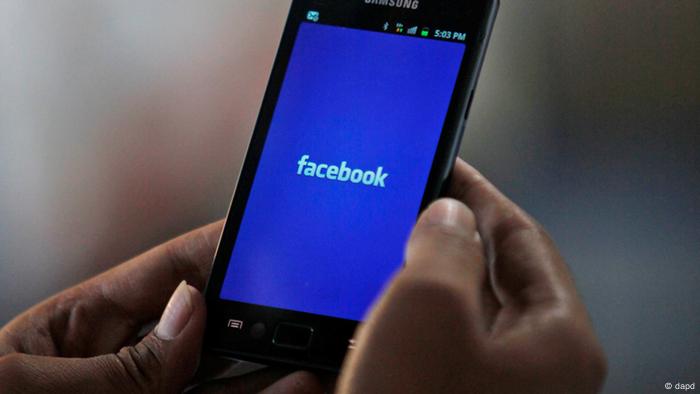An Indian man holds a smartphone showing Facebook